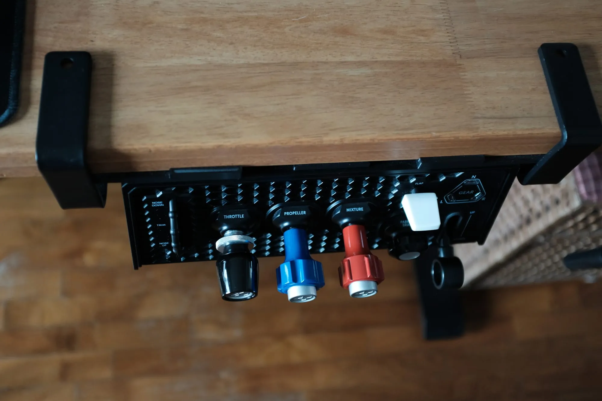 The Sierra TPM Module mounted flat beneath a desk, held by a black bracket at each end, with the trim wheel, three vernier levers and the flap toggle facing down.
