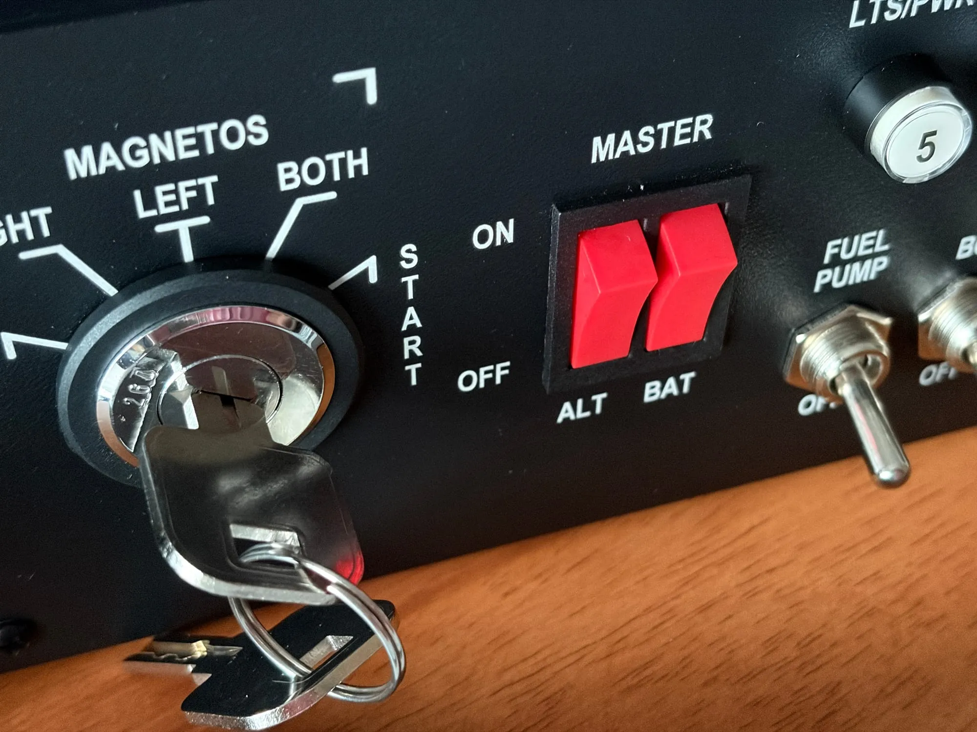 Close view of the ignition key in the Meza panel: the MAGNETOS dial marked LEFT, BOTH and START, the red master rockers and the fuel pump toggle