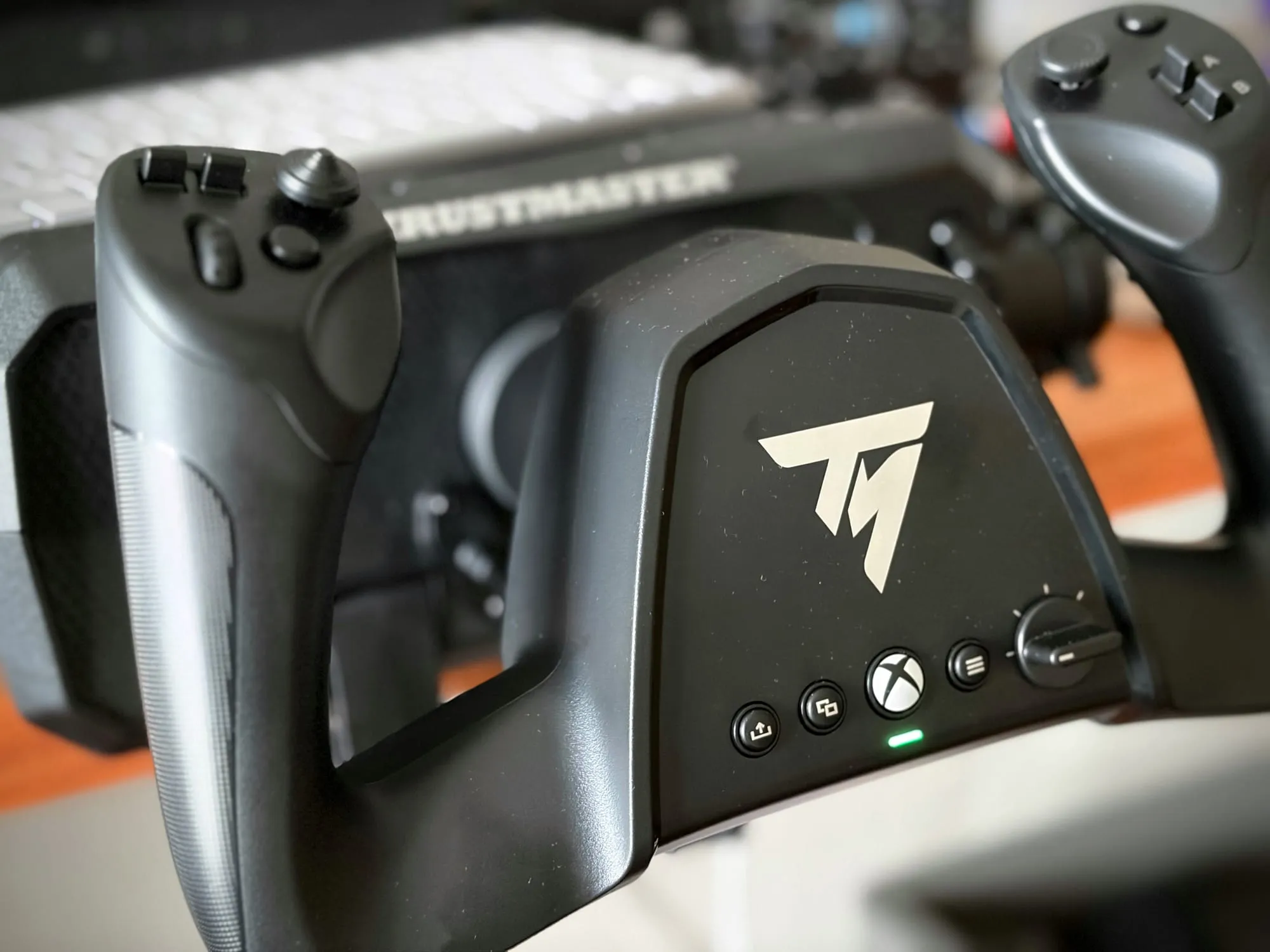 Close-up of the Sky Yoke hub: silver Thrustmaster logo, four round buttons including an Xbox button, a notched rotary dial and a small green indicator light.