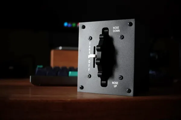 The Meza trim wheel panel straight on: scalloped black wheel in its slot with NOSE DOWN, TAKE OFF and NOSE UP labels on a charcoal metal panel, desk blurred behind
