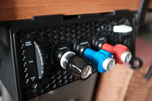 Close-up of the Honeycomb Sierra TPM Module under a desk: the honeycomb faceplate with the trim wheel and black, blue and red vernier levers for throttle, propeller and mixture.