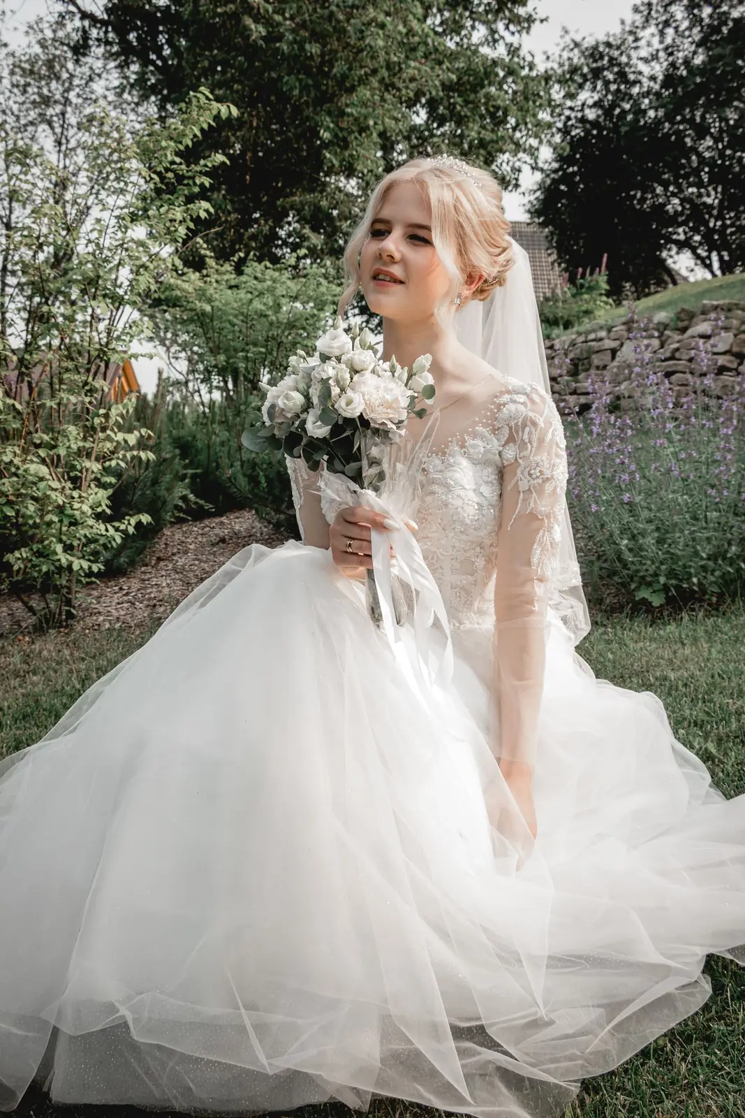 Elegant bride in a white wedding dress holding a bouquet in an outdoor garden setting.