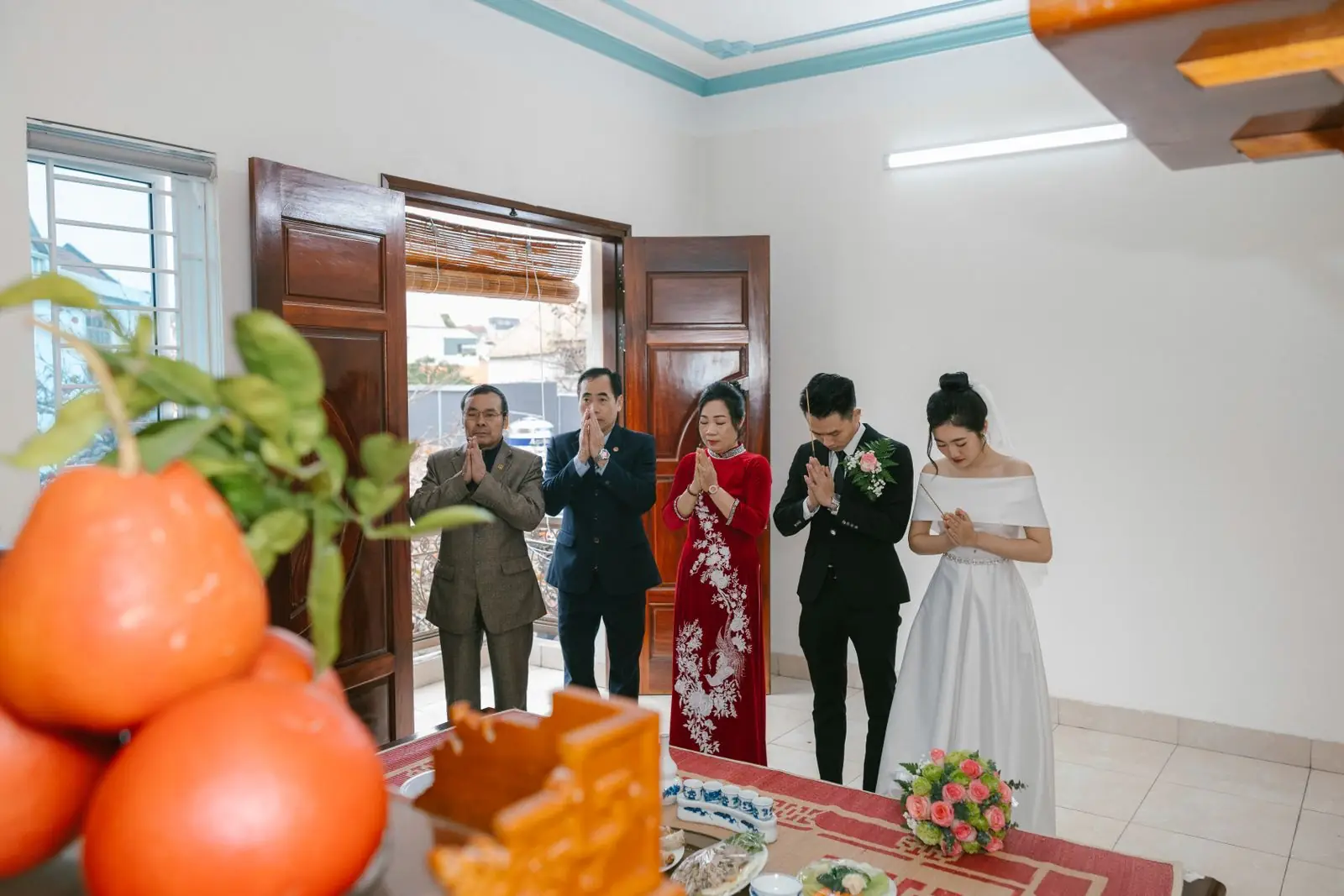 A group participating in a traditional wedding ceremony with prayers, indoors, featuring vibrant attire and cultural elements.