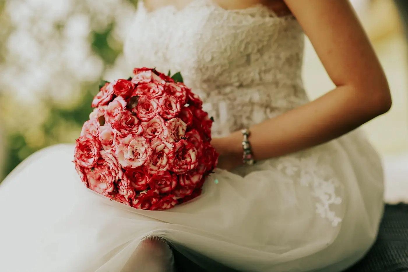 Bride holding a lush bouquet of pink roses in an elegant white gown, perfect for wedding themes.