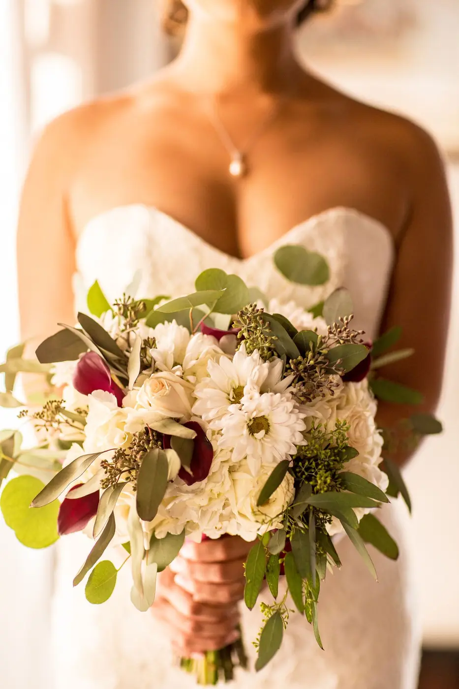 Close-up of a bride holding a beautiful floral wedding bouquet indoors.