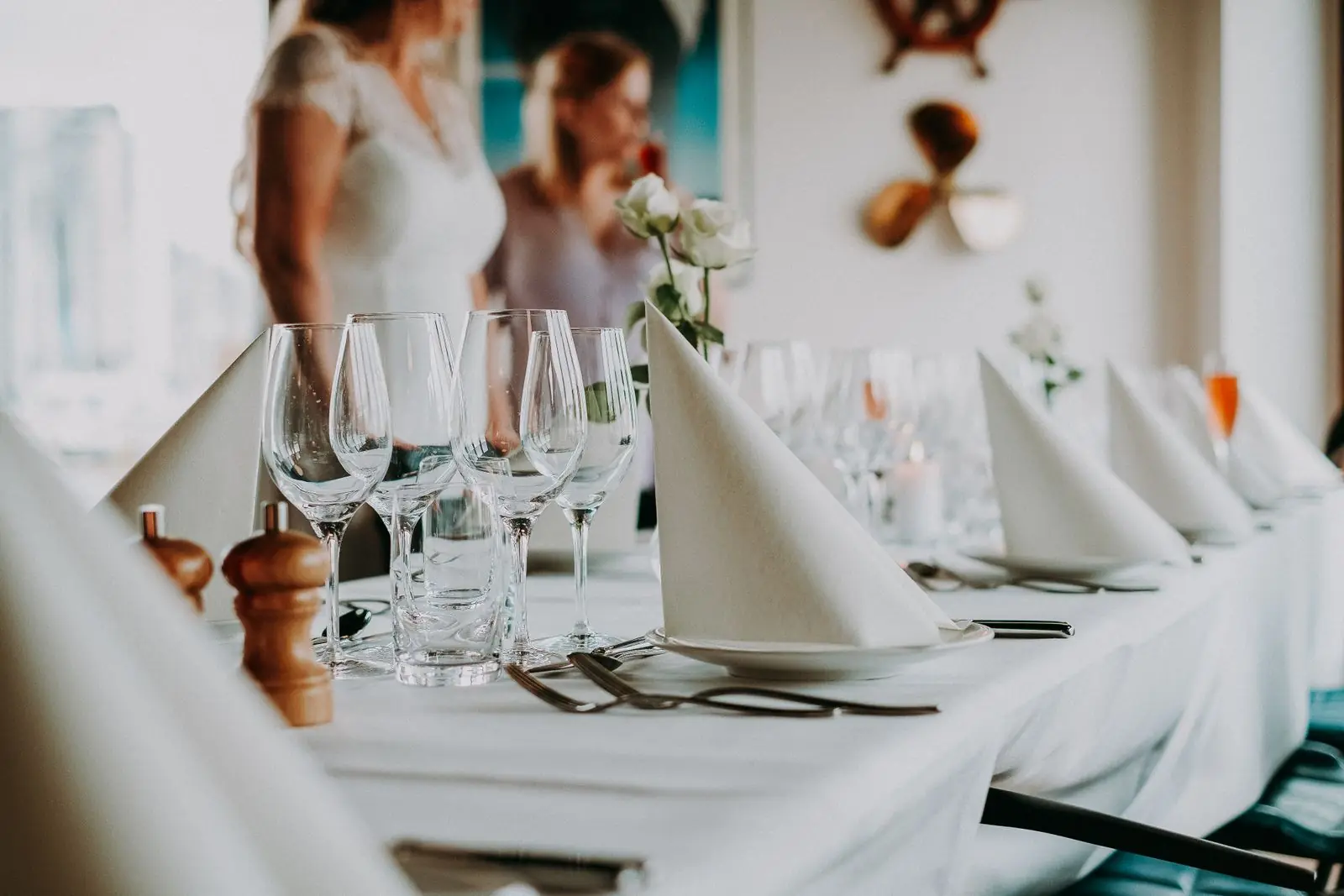 Served table with wineglasses and cutlery placed near napkins on white cloth against blurred people on background during wedding celebration in restaurant