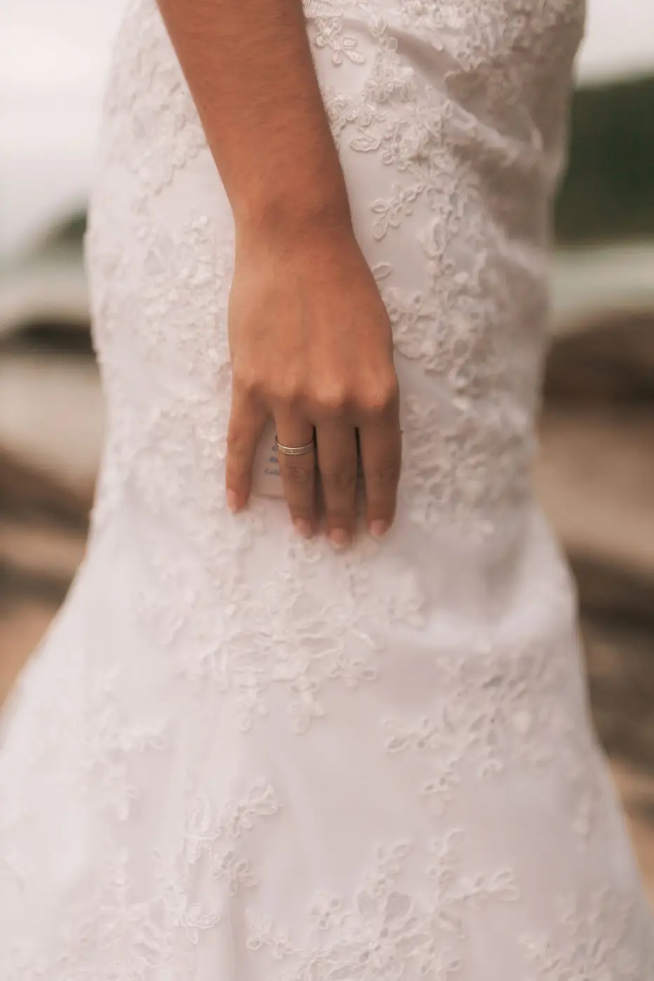 Close-up of a bride's hand on a lace wedding dress, showcasing fine details and ring.