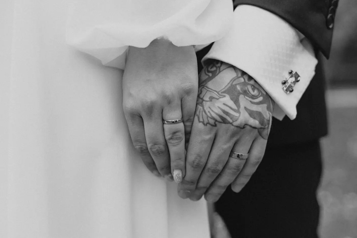 Close-up shot of married couple holding hands with rings, showcasing tattoos.