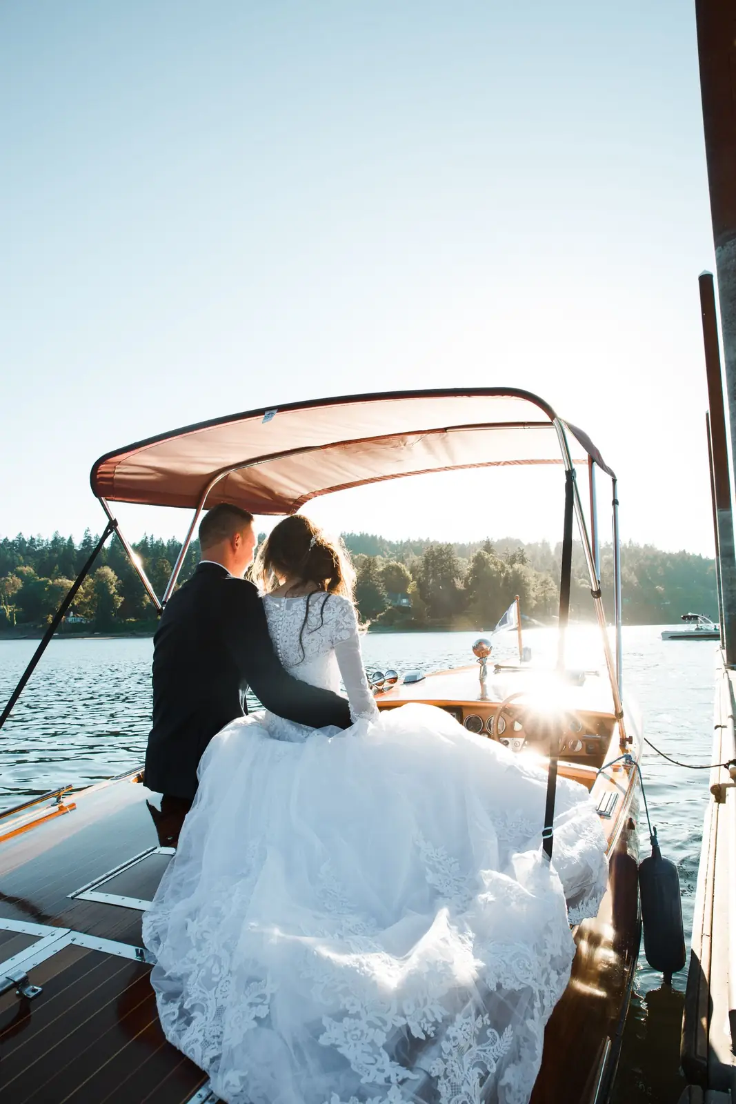 Bride and groom sitting on a boat enjoying a picturesque water view on a sunny day.