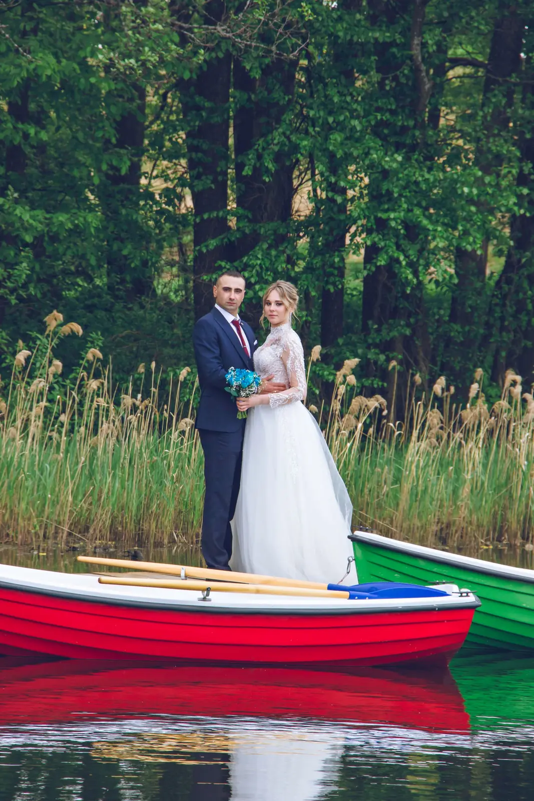 Bride and groom posing on a colorful boat by a serene lakeshore. Perfect wedding or romance theme.