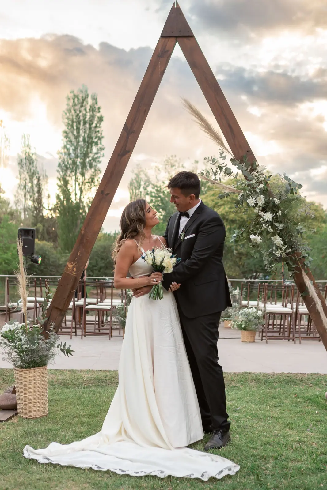Bride and groom embracing outdoors under a floral arch in Mendoza, Argentina.