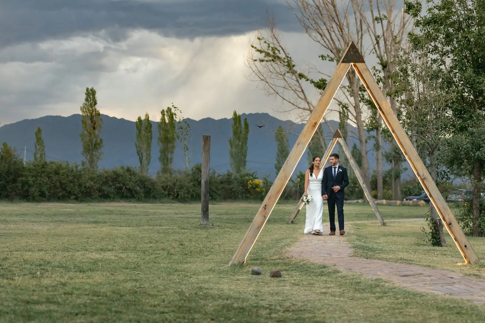 Newlyweds walking under wooden arch in scenic park setting, perfect for wedding themes.