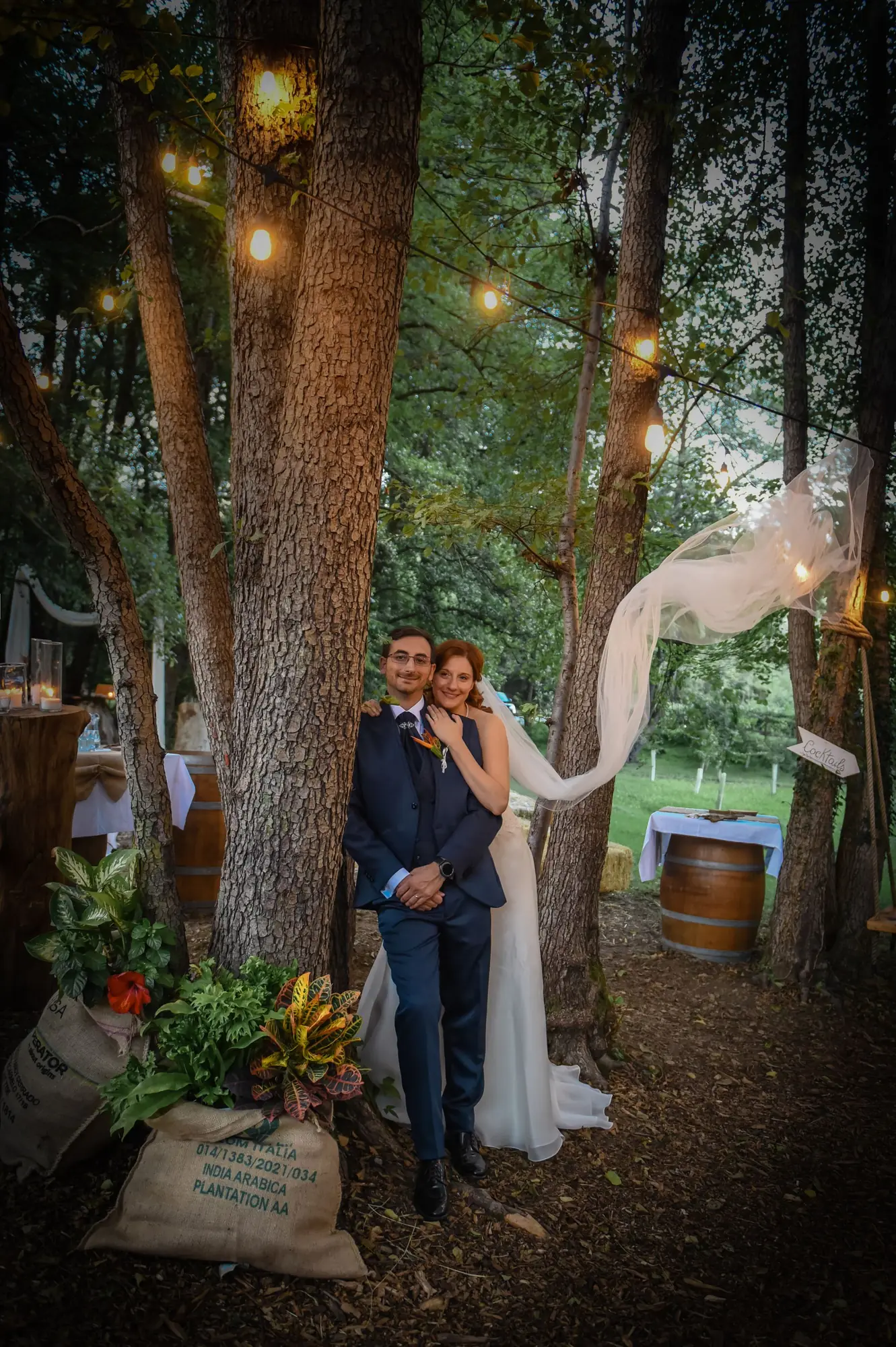 A bride and groom embrace outdoors under enchanting fairy lights.