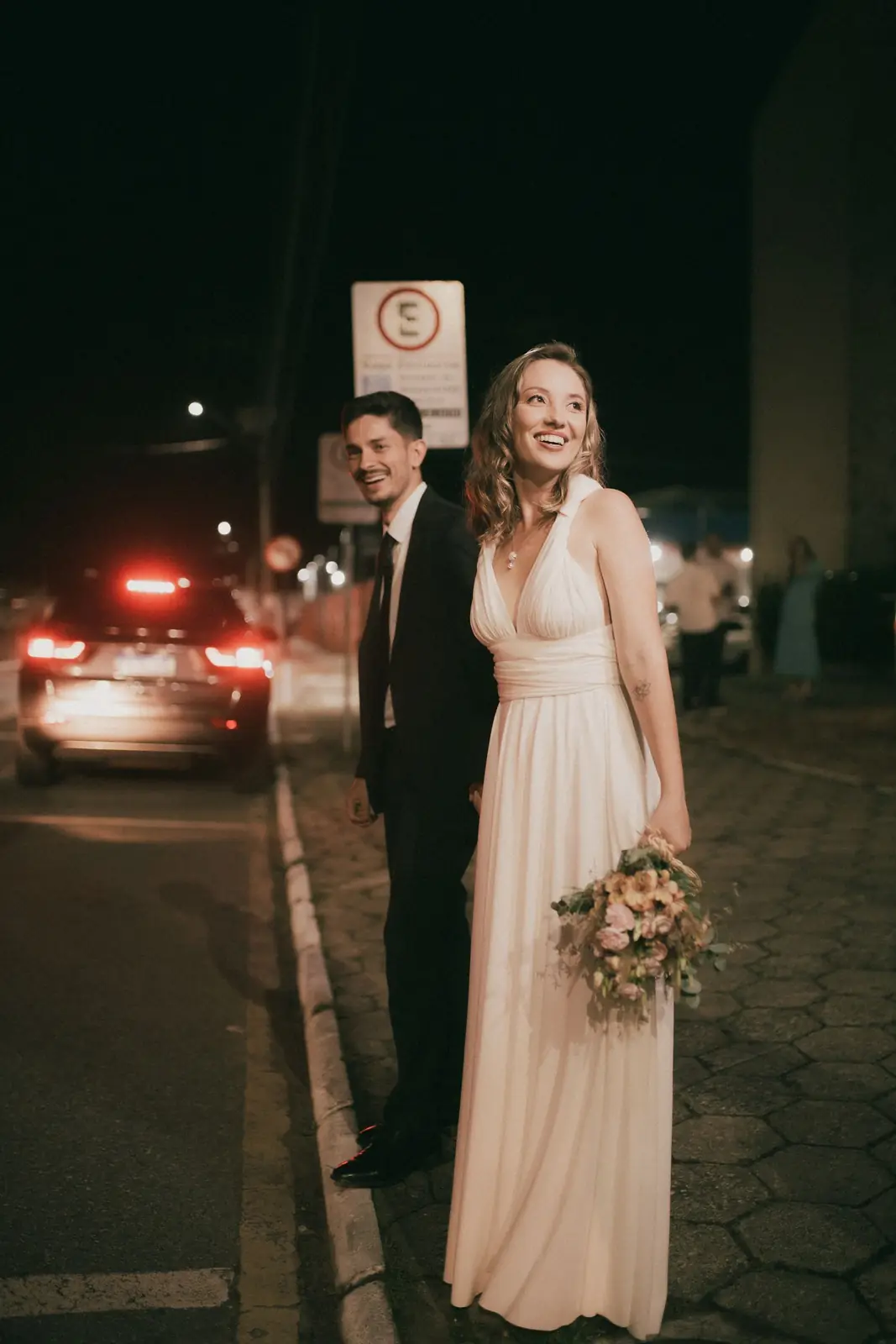 A smiling bride and groom pose elegantly on a city street at night, showcasing togetherness.
