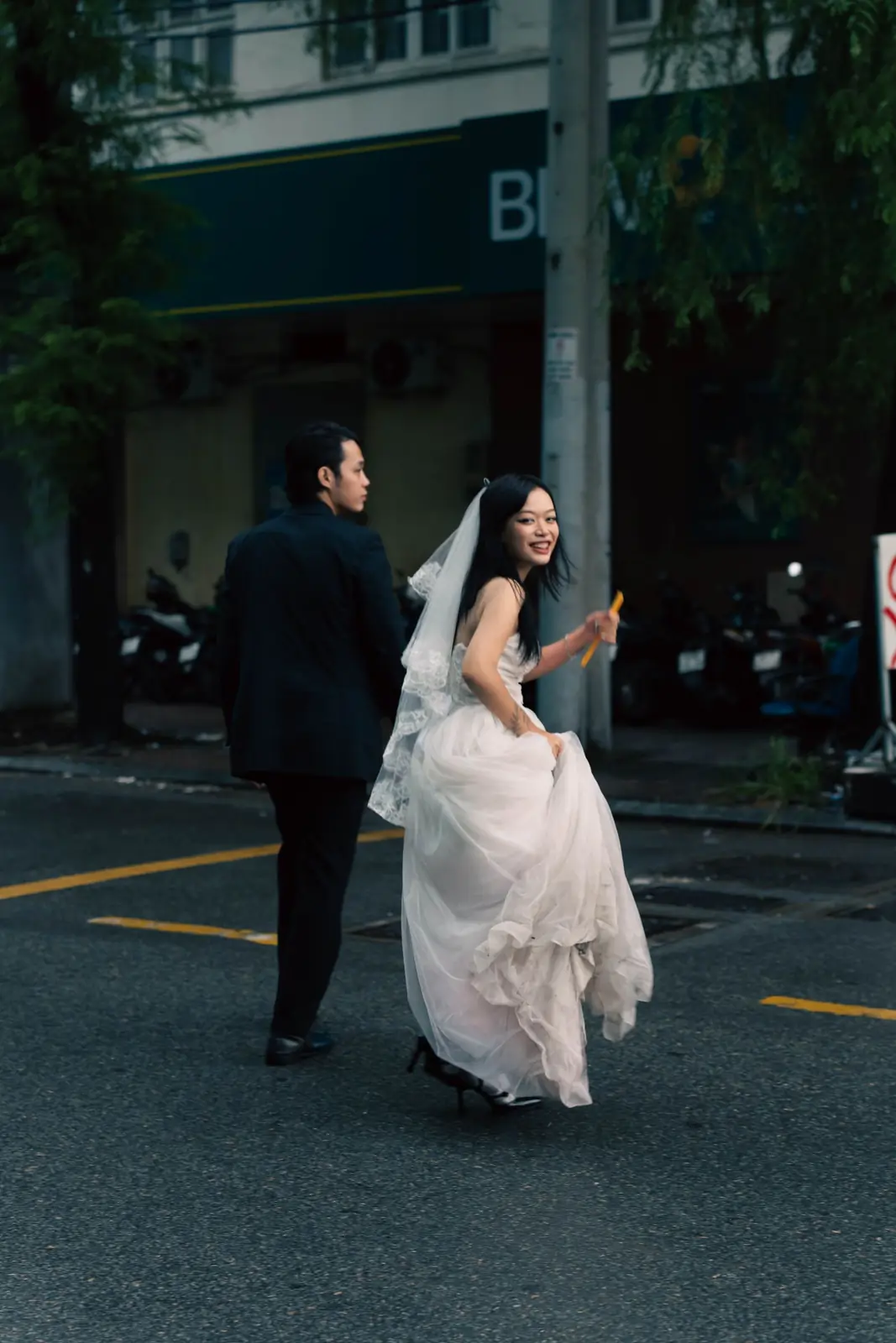 Joyful bride and groom in wedding attire walking on city street.