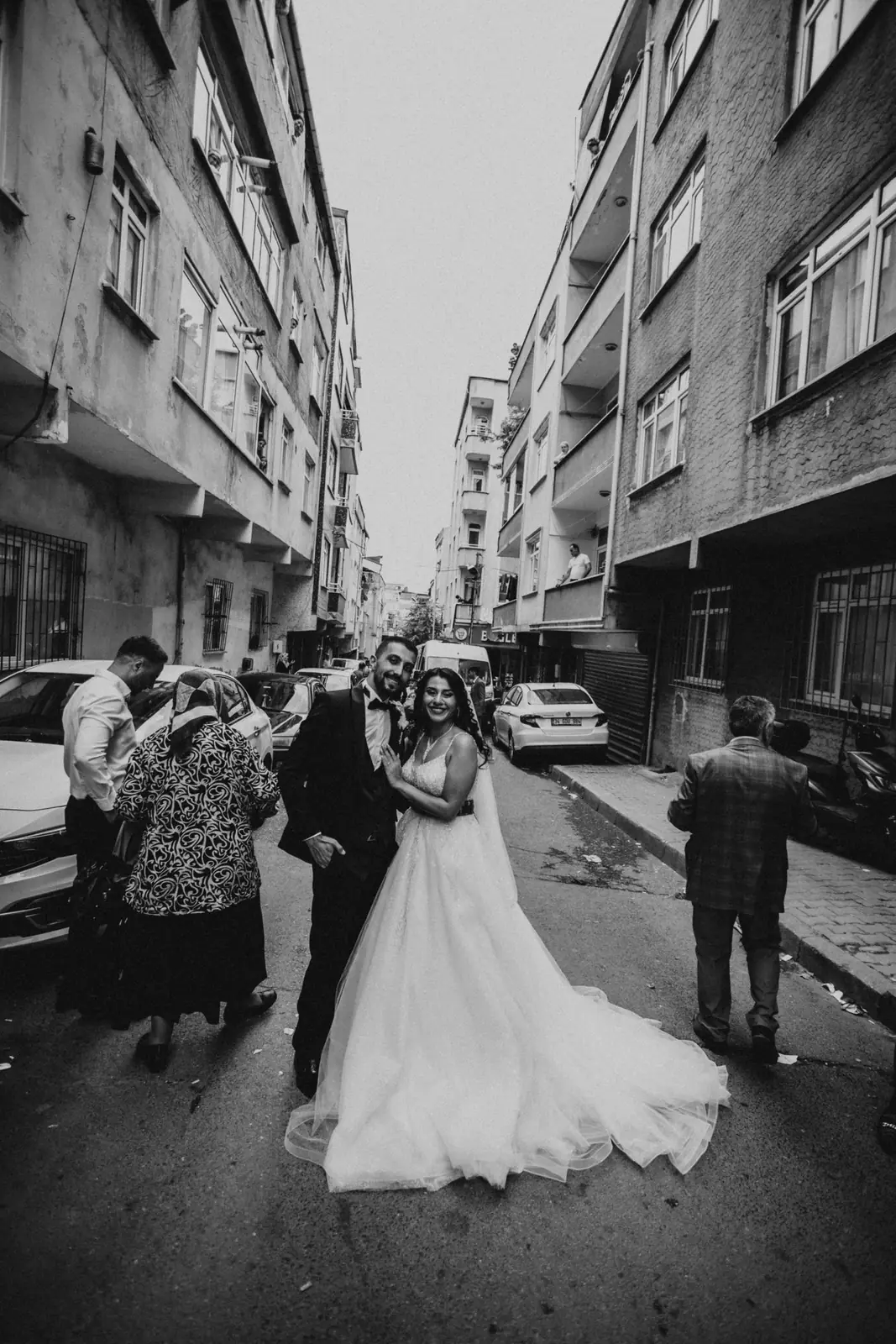 Black and white photo of a newlywed couple posing on an urban street amidst city buildings.