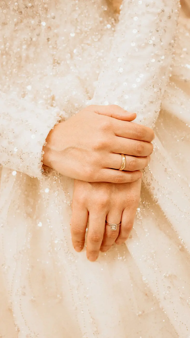 Close-up of a bride's hands showcasing wedding rings and elegant sequined dress.