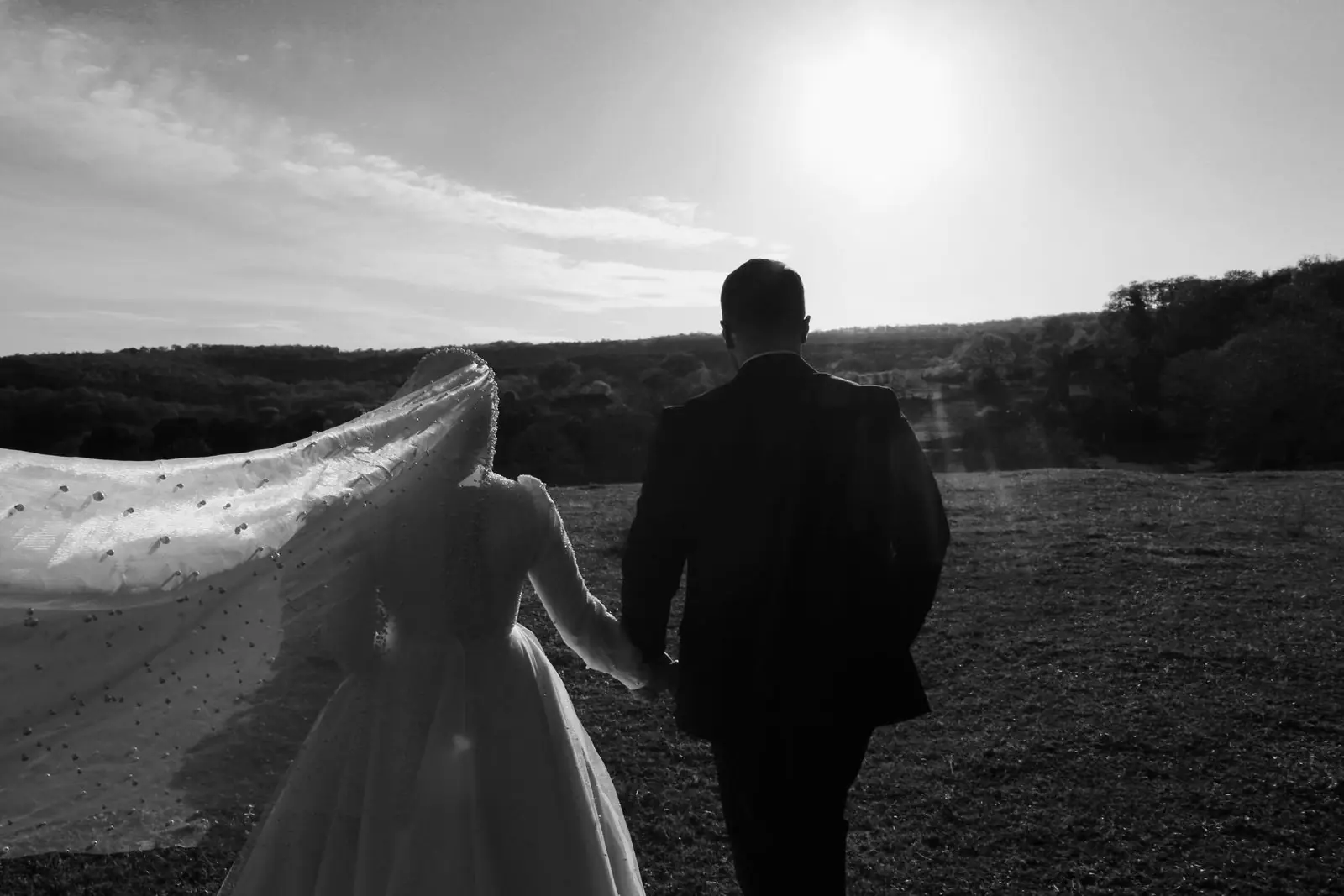 Black and white photo of a wedding couple walking together in a sunny outdoor setting.