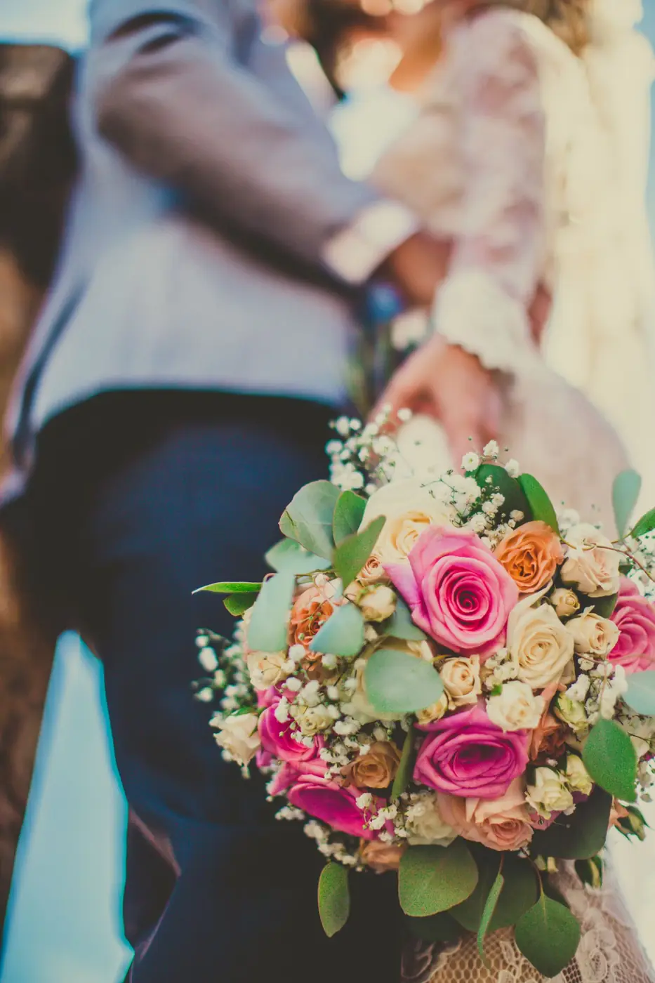 Close-up of a bride and groom embracing with a vibrant bouquet in focus, signifying love and celebration.