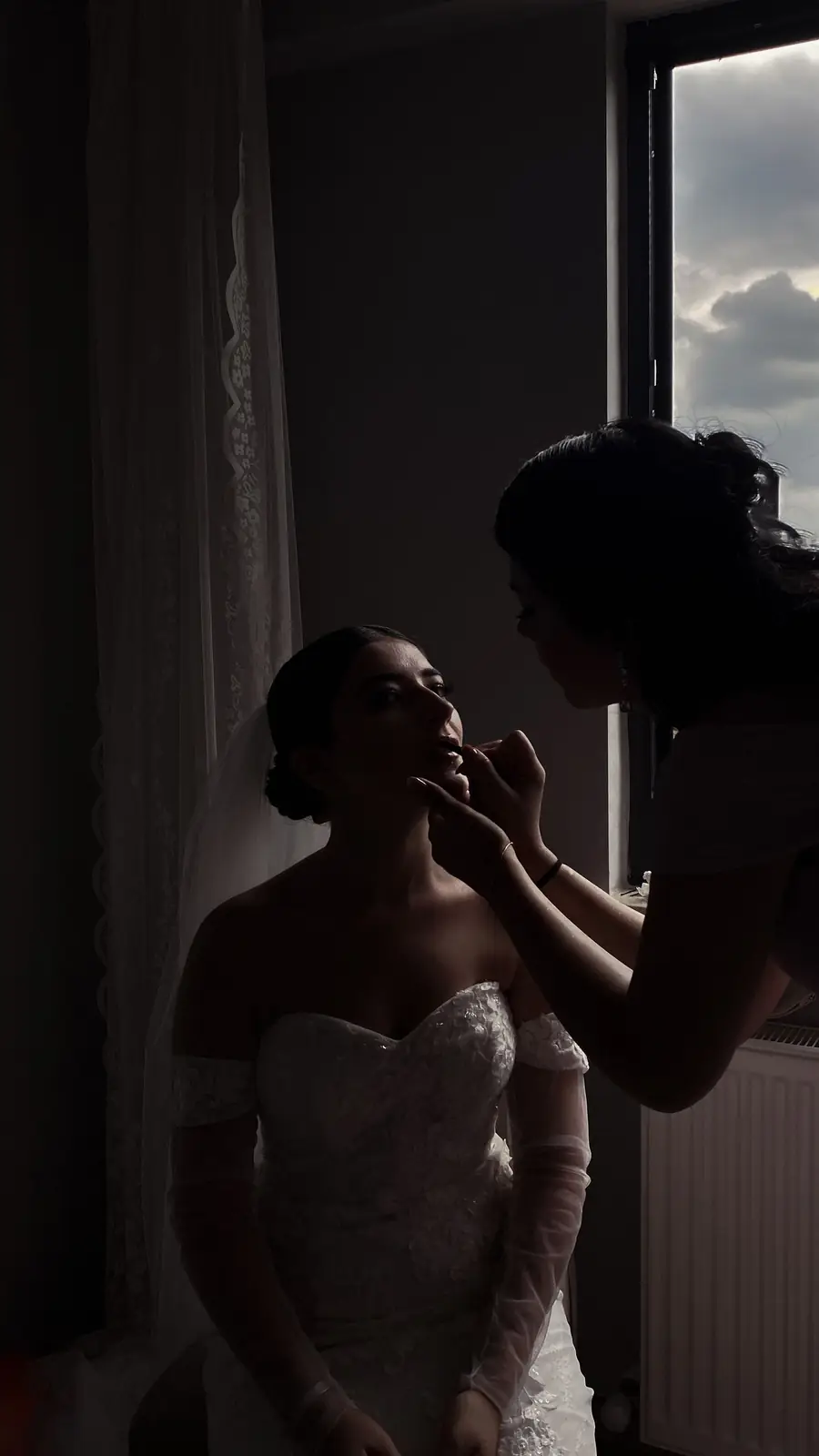 A bride getting her makeup done near a window, highlighting elegance and preparation before her wedding.