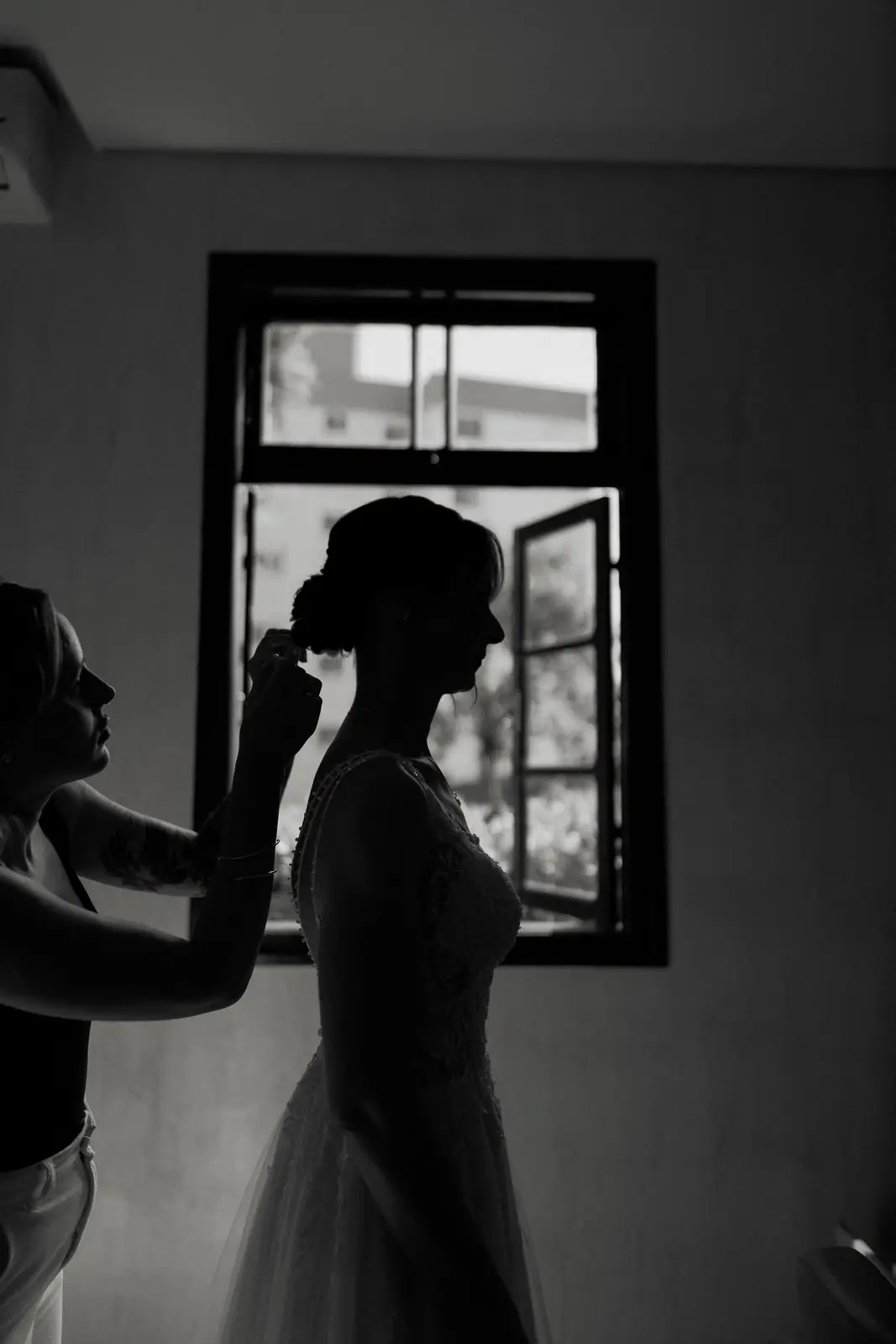 Silhouette of a bride getting ready by a window, elegant and timeless.