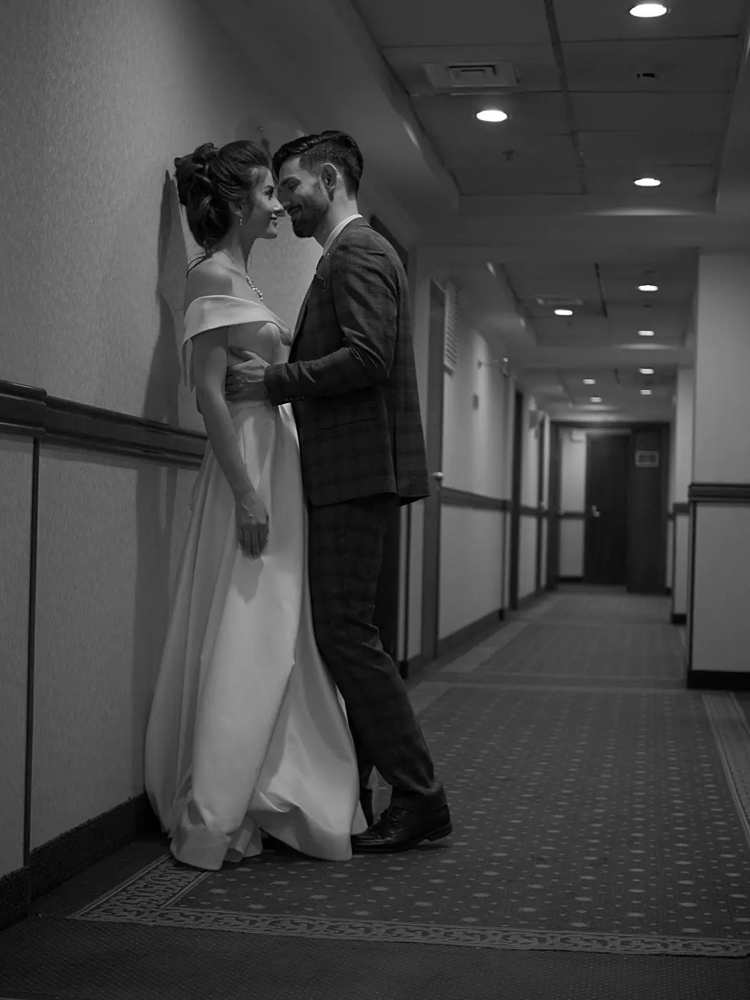 Artistic black and white photo of a couple in wedding attire standing in a hallway.