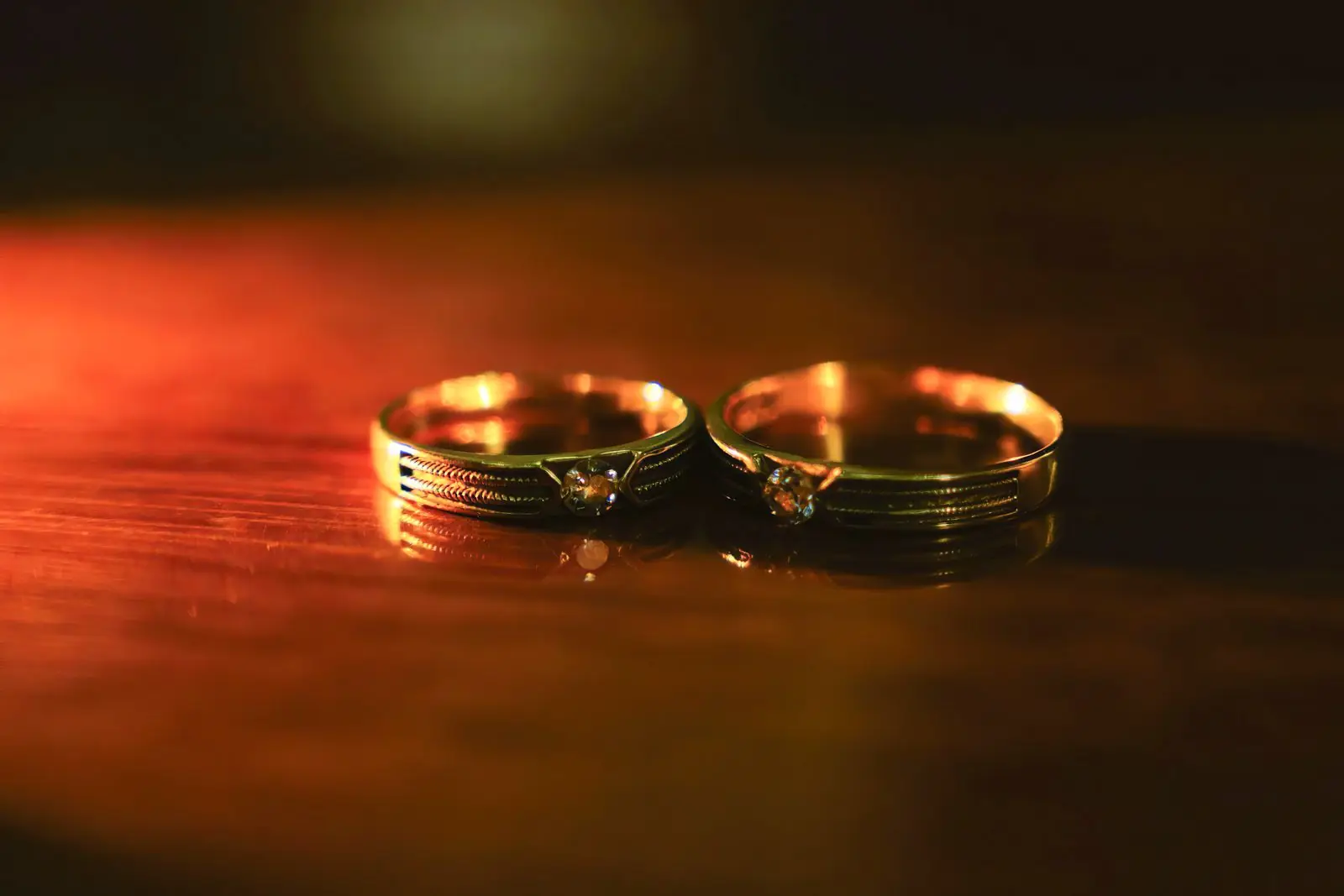 Two golden wedding rings with diamonds sparkle on a wooden surface, capturing romance.