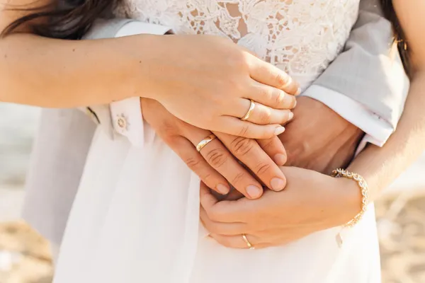 Close-up of a bride and groom's joined hands wearing gold wedding rings.