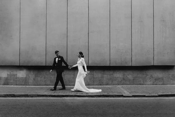 Black and white photo of bride and groom walking along an urban street in Lima, creating an elegant and timeless scene.