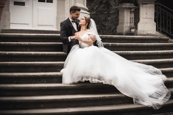Bride and groom sitting together on stone steps outside a historic building.