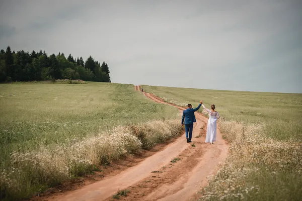 Bride and groom raising their joined hands as they walk along a country path.
