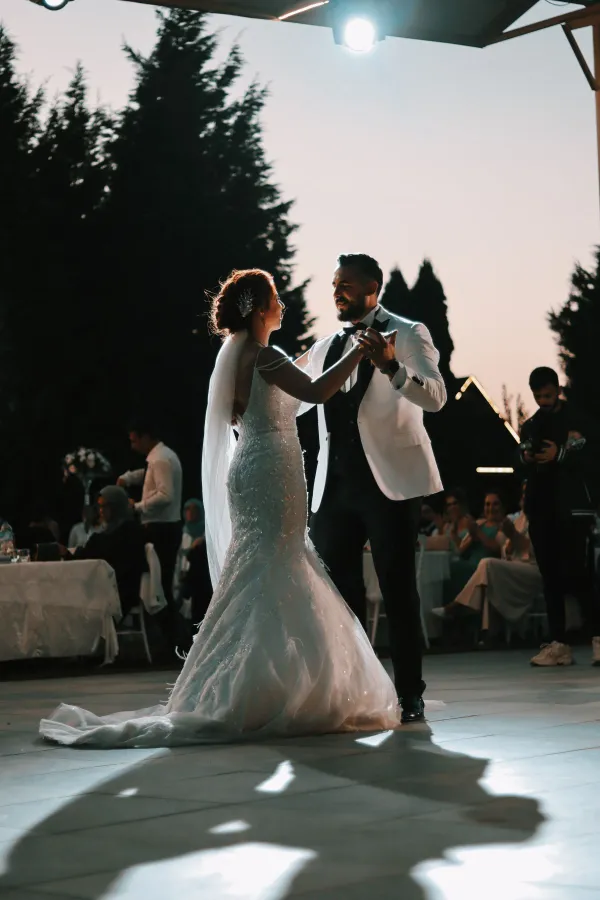 Newlyweds share a romantic dance under the evening sky, surrounded by guests.