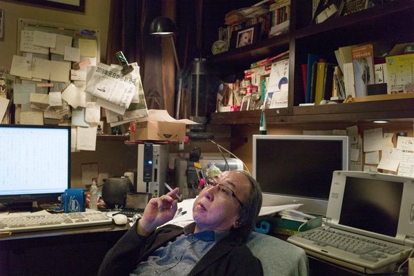 Hideo Yokoyama smoking a cigarette, surrounded by paper and computers