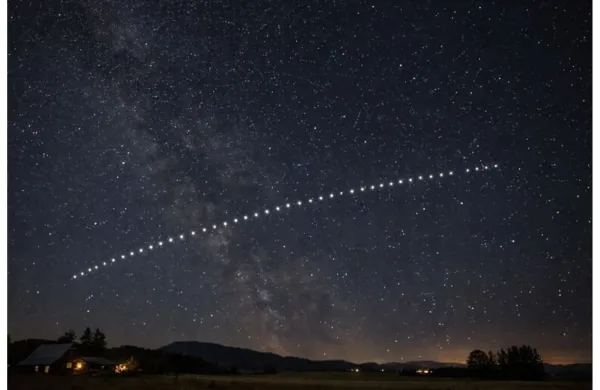 Starlink satellites appearing in a straight line across the night sky above a rural area.