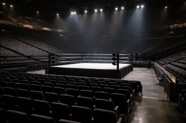 Empty indoor wrestling arena with ring and lighting setup, photographed before a live event with no crowd present.