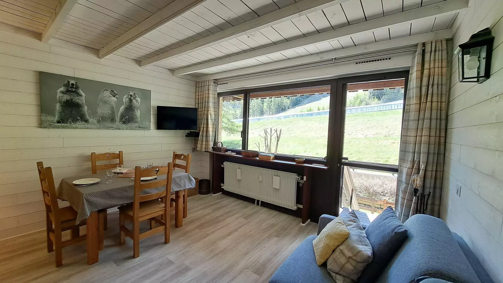 Séjour lumineux d’un appartement de montagne avec coin repas en bois, canapé confortable et grande baie vitrée donnant sur la nature.