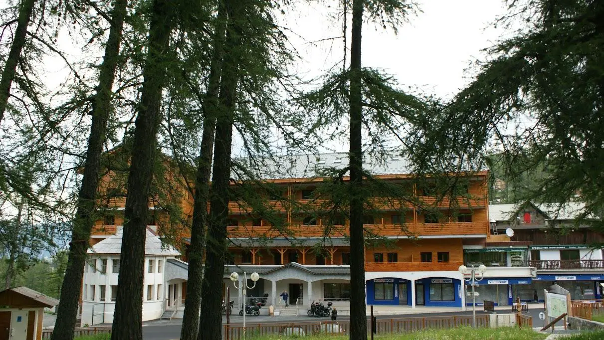 Façade en bois de la résidence Adonis Valberg, nichée derrière les arbres dans un cadre naturel et paisible.