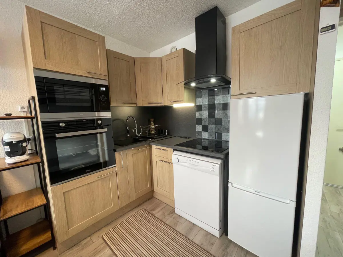 Cuisine moderne et fonctionnelle avec électroménager intégré, meubles en bois clair et crédence carrelée dans un studio de montagne.