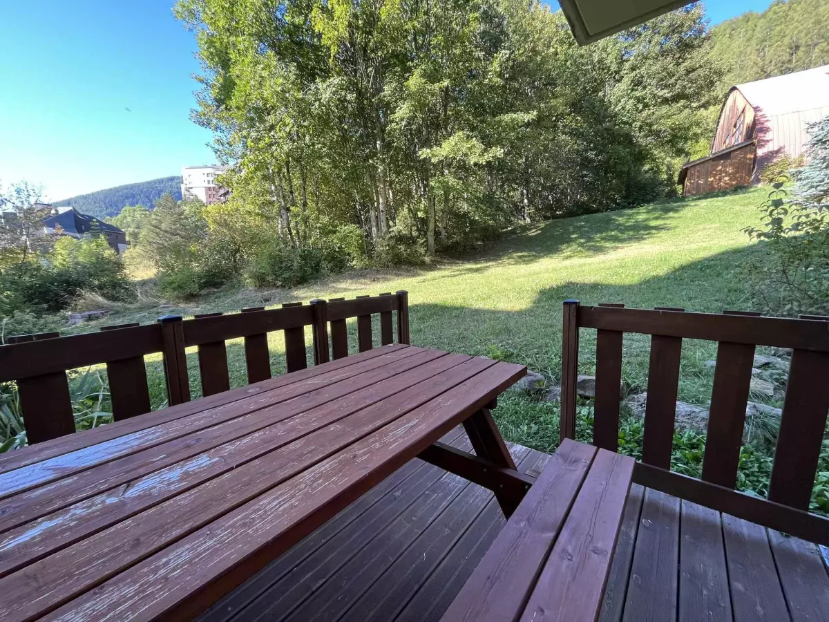 Terrasse en bois avec table de pique-nique donnant sur un jardin verdoyant, idéale pour profiter d’un repas en plein air à la montagne.