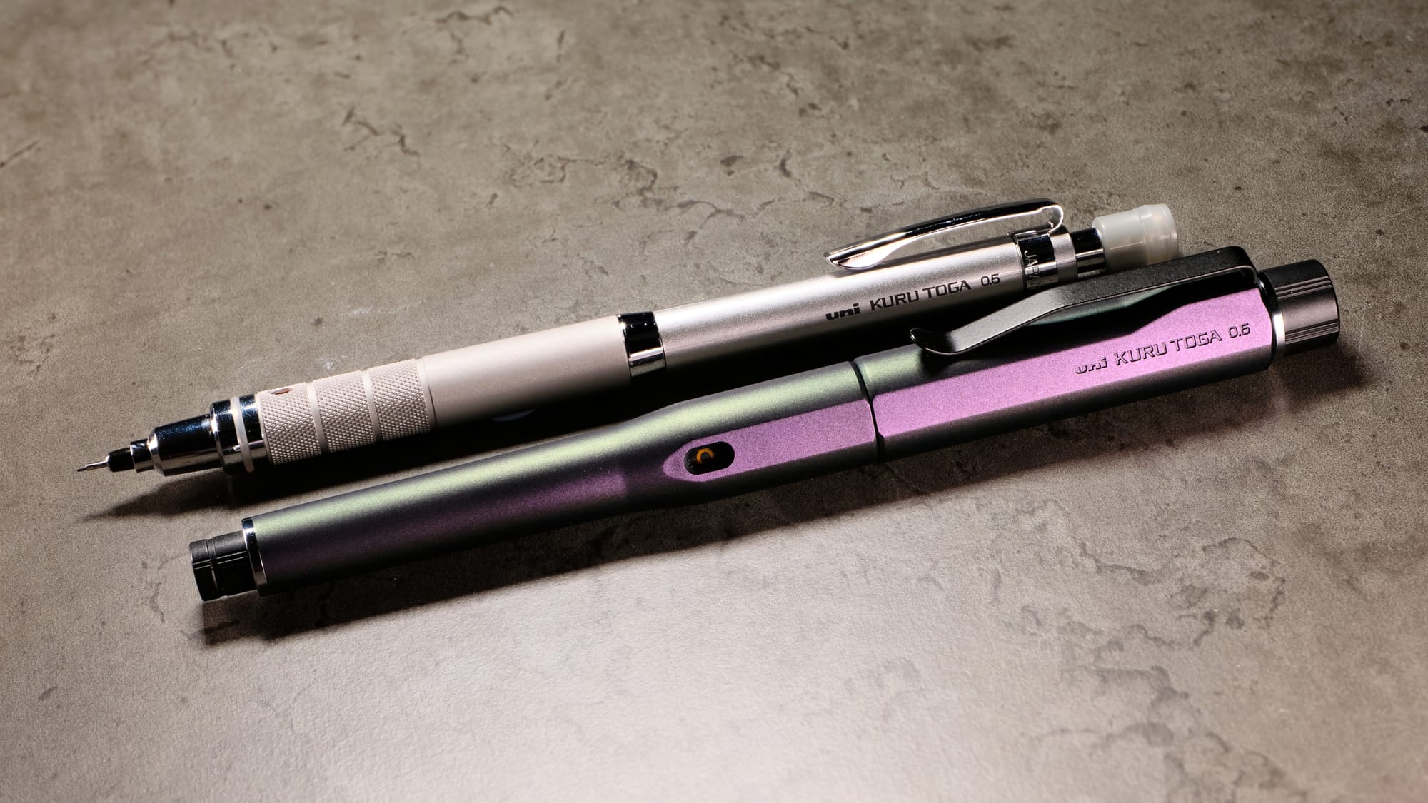 Photo of the Uni Kuru Toga Roulette & Dive mechanical pencils on a marbled grey background