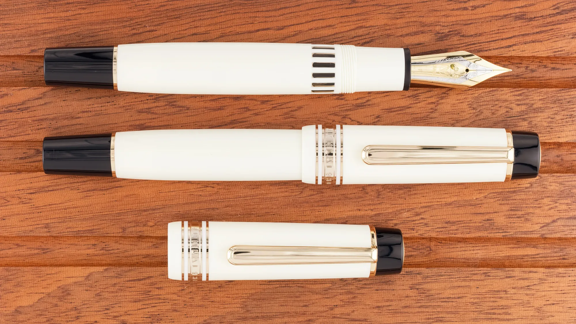 Overhead photo of a very large ivory & black fountain pen on a wooden tray. The pen is shown capped and uncapped.