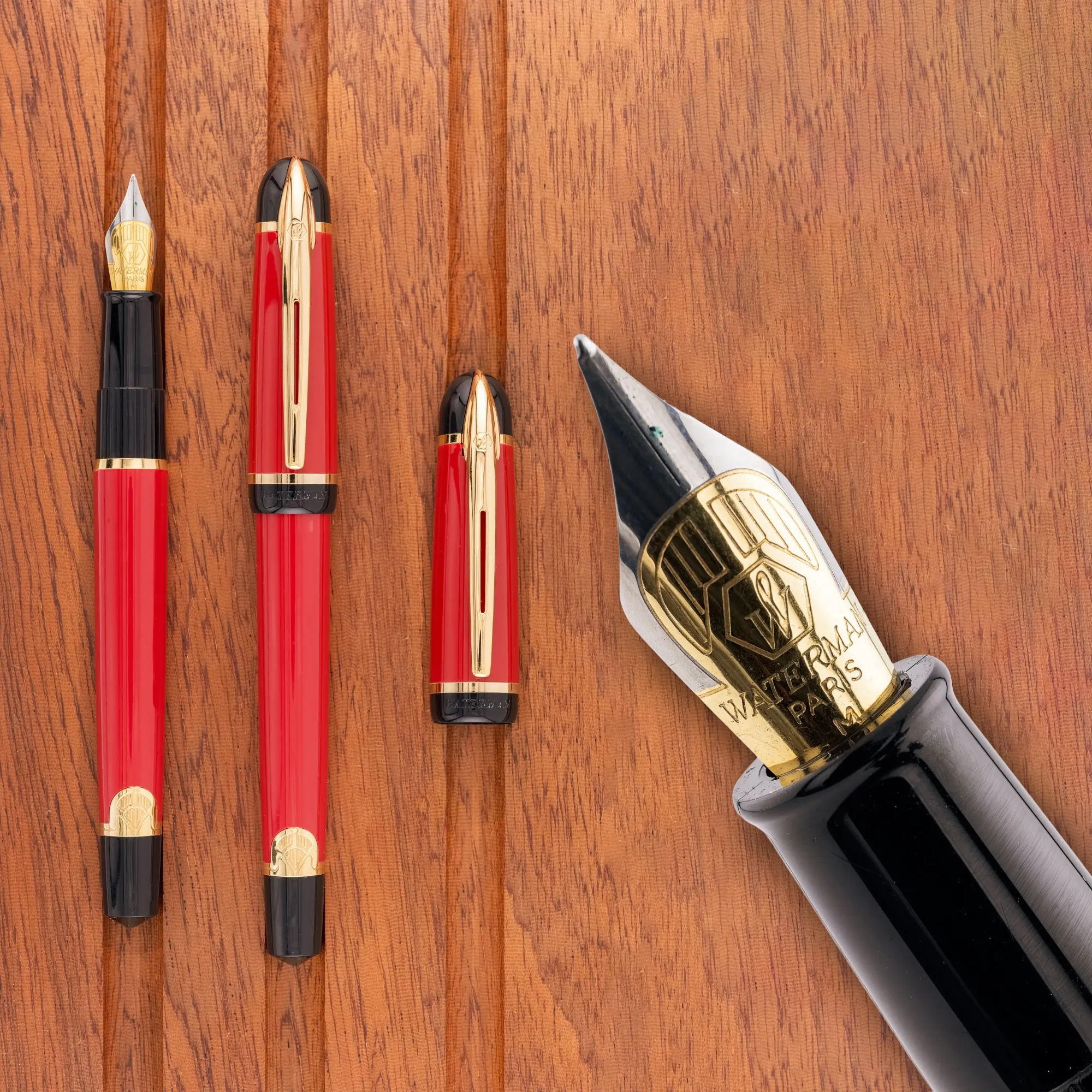 Overhead photo of a red & black with gold trimmed art deco-style fountain pen on a wooden tray. The pen is shown capped and uncapped, along with a close-up of the nib.