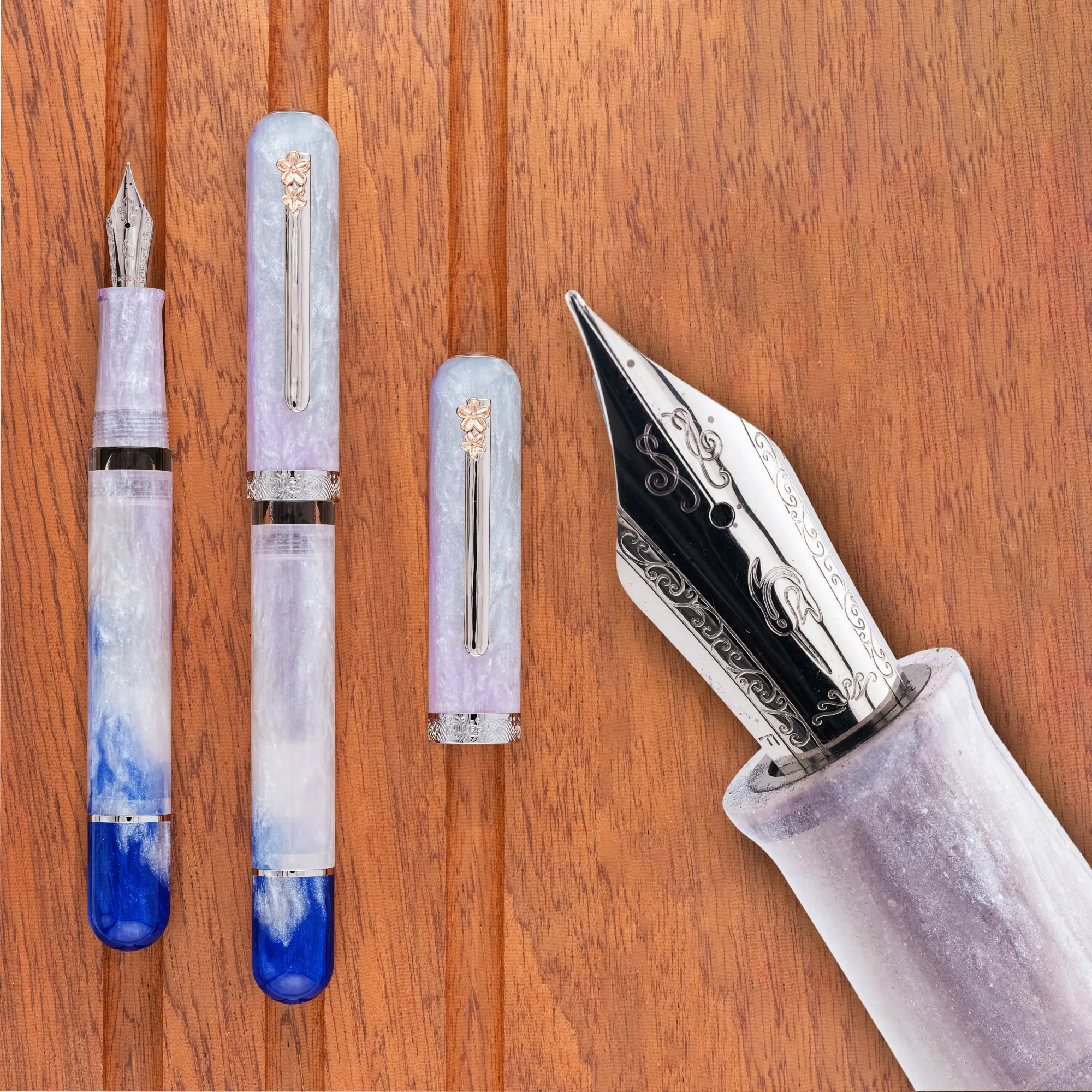 Overhead photo of a sparkling white, blue, & pink acrylic, cigar-shaped fountain pen on a wooden tray. The pen is shown capped and uncapped, along with a close-up of the nib.