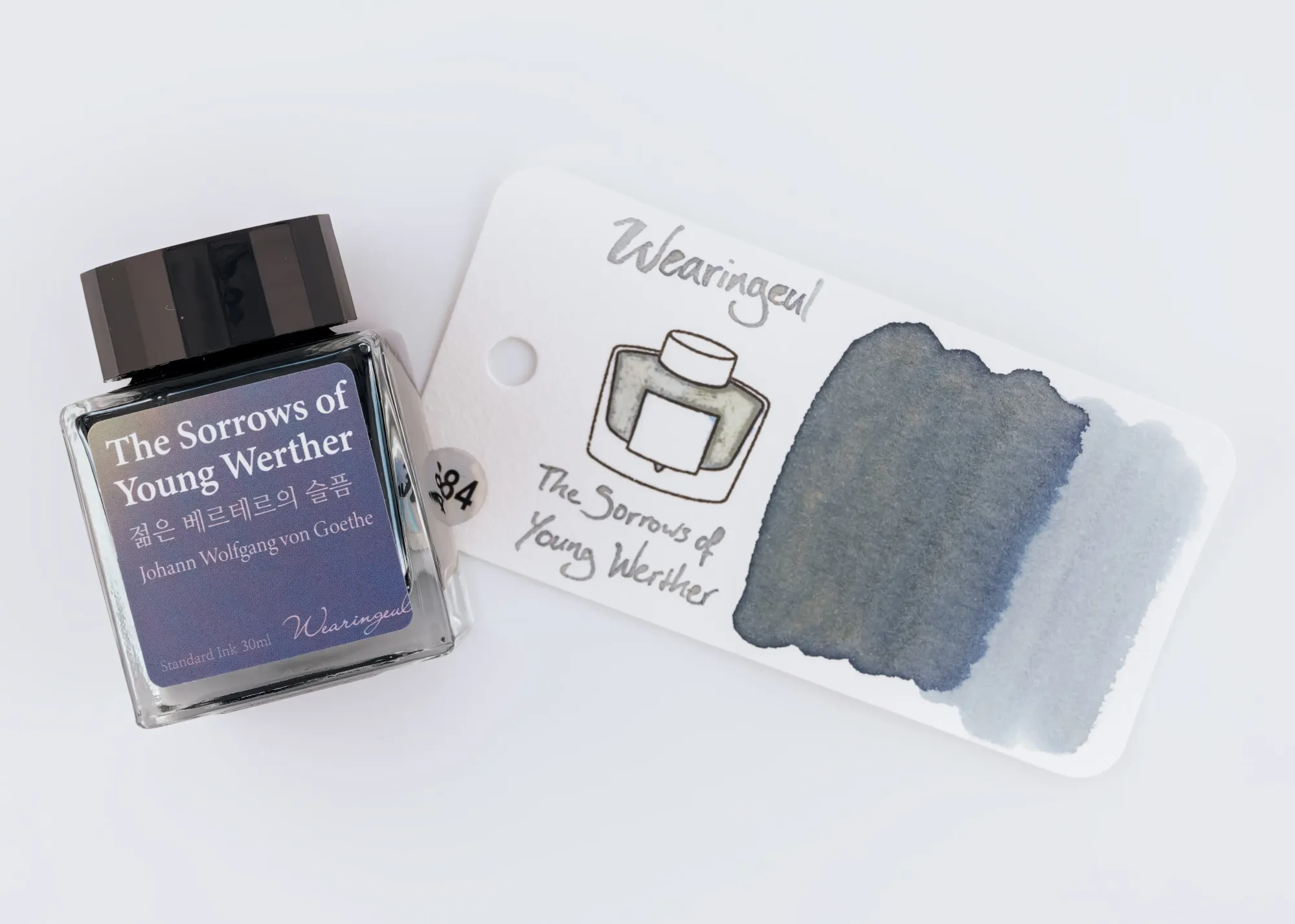 Overhead photo of a Wearingeul ink bottle next to a swatch of the blue-grey and yellow ink on a white background.