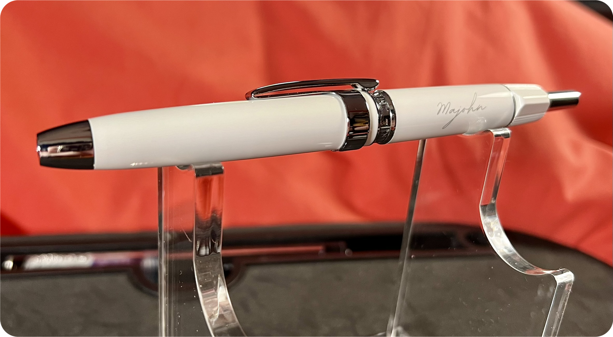 Photo of a thick, white retractable fountain pen on an acrylic stand with an orange & grey background