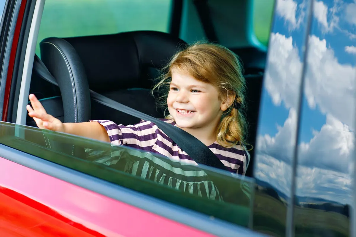 Fille adorable d’enfant en bas âge se reposant dans le siège d’auto et regardant par la fenêtre sur la nature et la circulati
