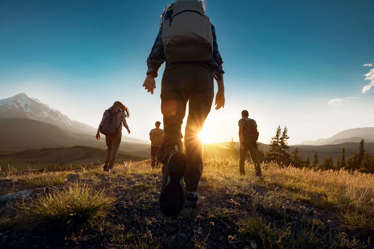 Group Of Sporty People Walks In Mountains At Sunset With Backpacks