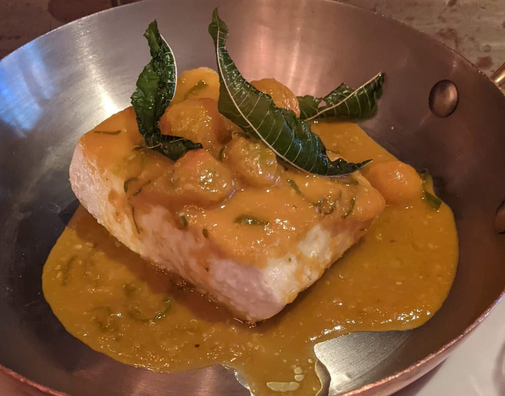 A filet of halibut in a silver dish, covered in a golden tomato sauce