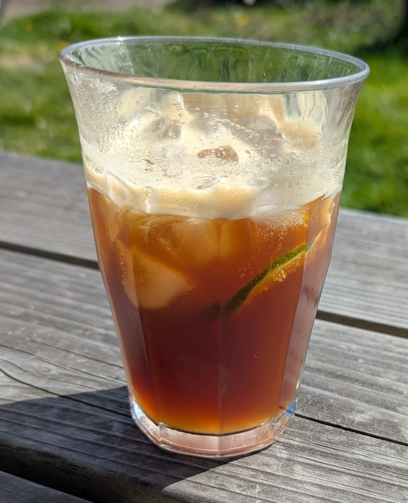A close-up of iced coffee and tonic water in glass on a sunny deck