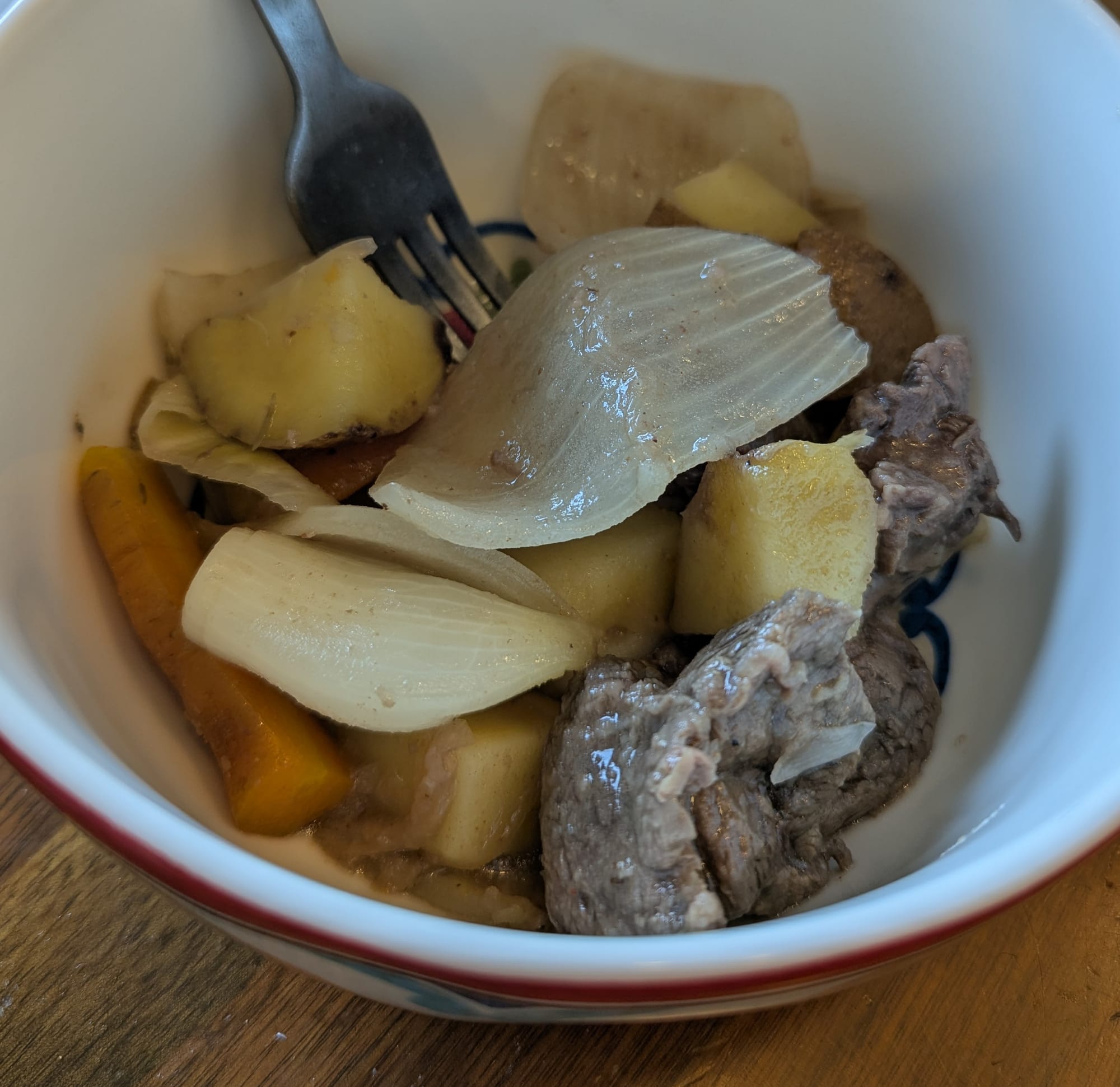 A bowl of stew with meat, carrots, potatoes, and onions
